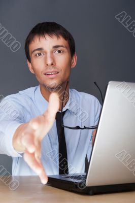 Businessman gives a handshake. Sitting near his laptop at his de