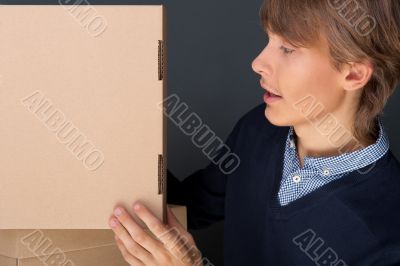 Portrait of young man leaning on box against grey wall. He is st