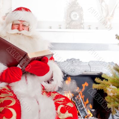 Santa sitting at the Christmas tree, near fireplace and reading 