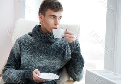 Portrait of a young man drinking coffee while sitting on armchai
