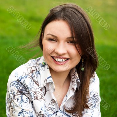 Closeup portrait of pretty young woman resting on grass and smil