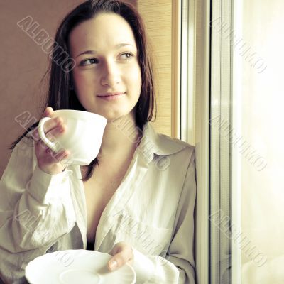 Portrait of cosy young girl standing near a window at home