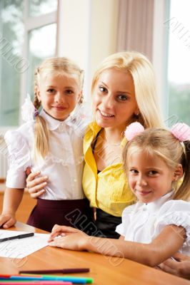 Young pretty teacher helping her little students in classroom