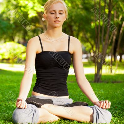 Portrait of young beautiful couple sitting in lotus pose on gree