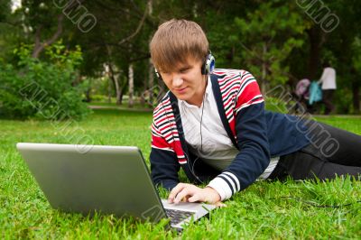 Student laying on grass and using laptop outside school