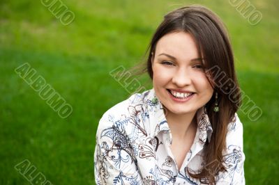 Closeup portrait of pretty young woman resting on grass and smil