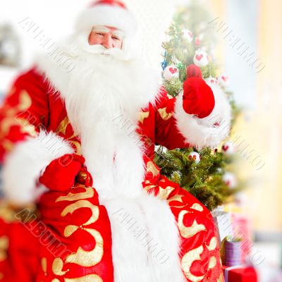 Santa sitting at the Christmas tree, near fireplace and looking 