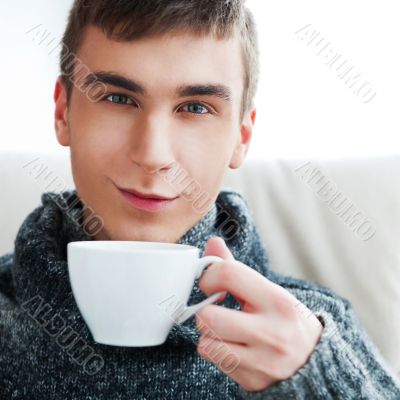 Portrait of a young man drinking coffee while sitting on armchai