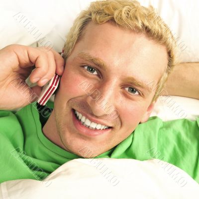 A man in his bed speaking cell phone and looking at camera