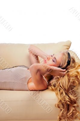 Young Girl enjoys listening music in headphones lying on sofa