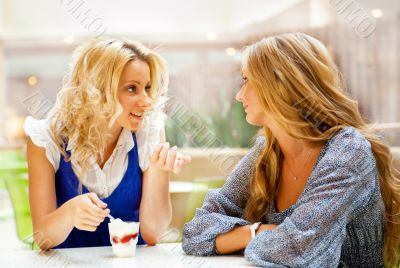 Two beautiful women drinking coffee and chatting at mall cafe.