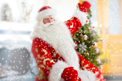 Santa sitting at the Christmas tree, near fireplace and looking 