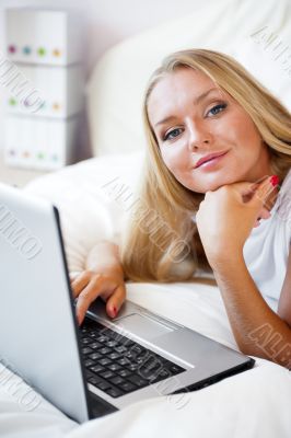 Smiling woman using a laptop while lying on her bed