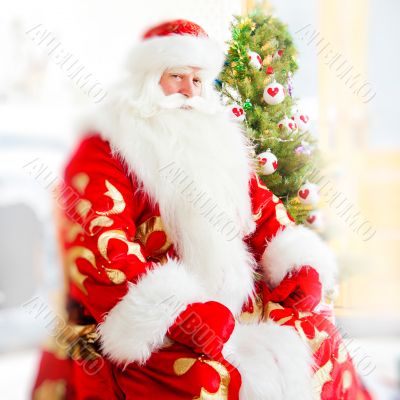 Santa sitting at the Christmas tree, near fireplace and looking 