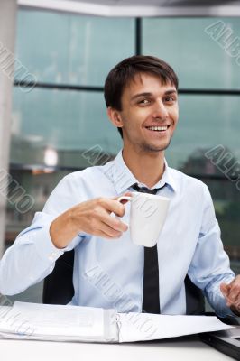 Young businessman having a morning coffee break, sitting at desk