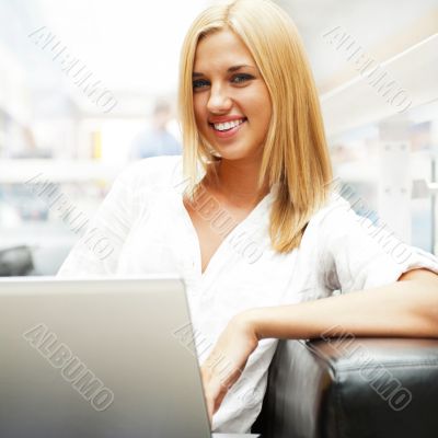 Portrait of happy blond woman using laptop at shopping mall cafe