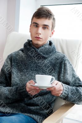 Portrait of a young man drinking coffee while sitting on armchai