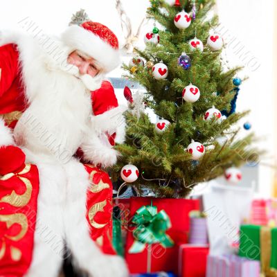 Santa sitting at the Christmas tree, fireplace and looking at ca