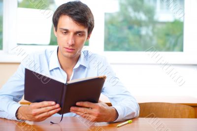 Portrait of a young handsome man with a book indoors