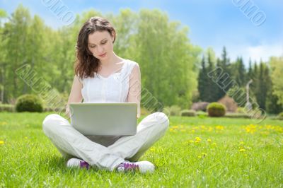 Young woman with laptop sitting on green gras
