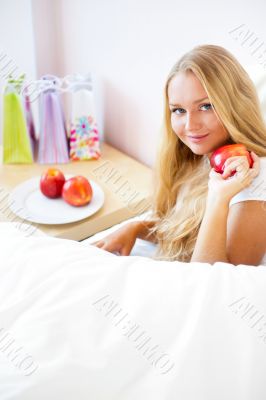 Young beautiful woman with apple in bed in the morning