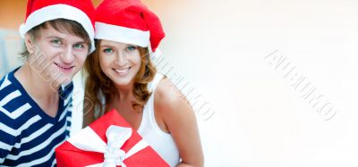 Young happy couple in Christmas hats standing together and holdi
