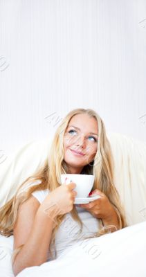 Smiling woman drinking a coffee lying on a bed at home or hotel.