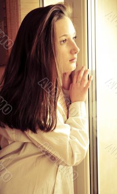 Portrait of cosy young girl standing near a window at home