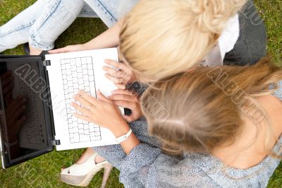 Portrait of two smiling women using laptop on a green meadow at 