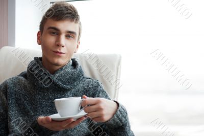 Portrait of a young man drinking coffee while sitting on armchai