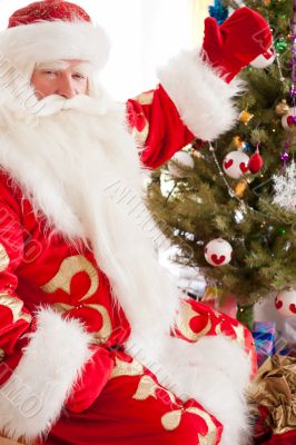 Santa sitting at the Christmas tree, near fireplace and looking 
