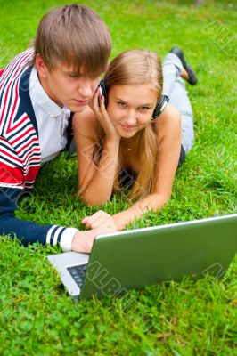 Happy young couple using laptop while lying on grass