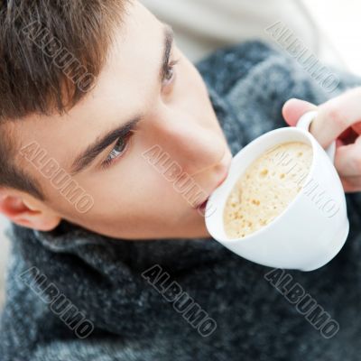 Portrait of a young man drinking coffee while sitting on armchai
