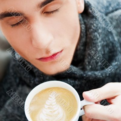 Portrait of a young man drinking coffee while sitting on armchai