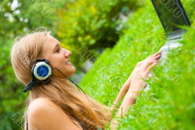 A smiling young girl with laptop outdoors listening music by hea