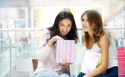 Two excited shopping woman resting on bench at shopping mall loo