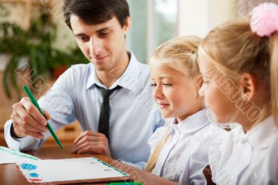 Teacher helping students with schoolwork in school classroom. Ho