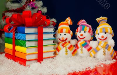 Stack of colorful books tied up with red ribbon and three snowme