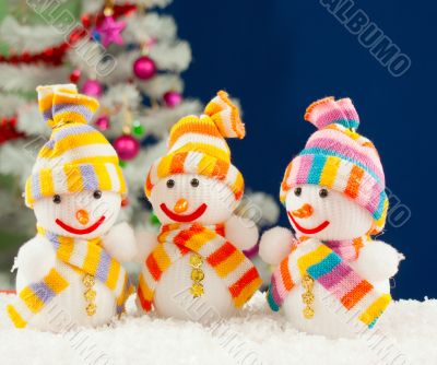 Three snowmen in front of the decorated white evergreen tree ove