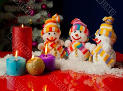 Three snowmen and burning candles over the blue background