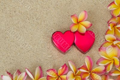 Frangipani /plumeria flower frame, with two red hearts on sand