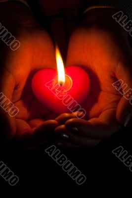 Human hands hold heart shaped burning candle