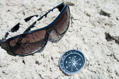 Sunglasses and compass in the sand