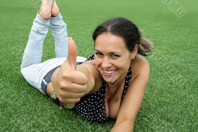 young woman lying on green meadow and shows up finger