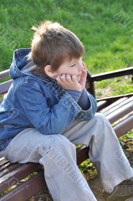 Pensive boy sitting on a park bench