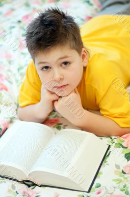 A boy reads a book in bed