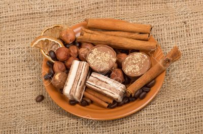 Sweets, cinnamon, nuts and coffee beans on a saucer, on burlap b