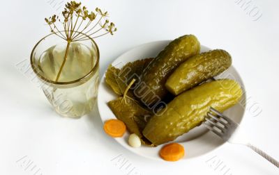 Cucumbers belong to the plate and standing next to a glass of pickle