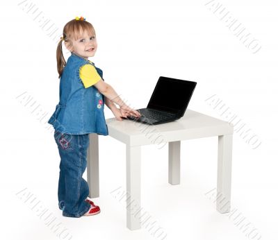 little girl in blue jeans standing at a table with a laptop