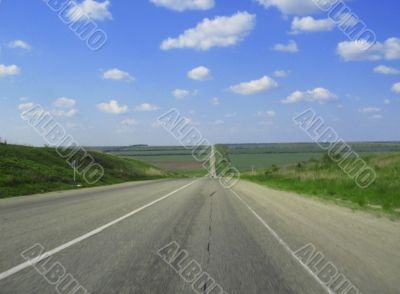 Wide highway and meadow. Clouds over and blue sky